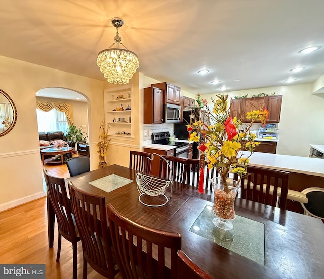 dining space featuring arched walkways, an inviting chandelier, baseboards, and light wood-style floors