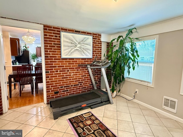 exercise area with visible vents, brick wall, baseboards, light tile patterned floors, and a notable chandelier