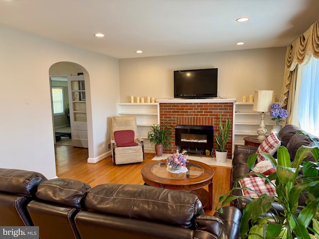 living room with a brick fireplace, recessed lighting, wood finished floors, and arched walkways