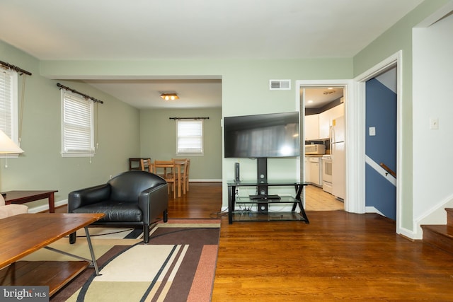 living area with visible vents, baseboards, wood finished floors, and stairway