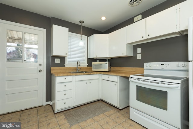 kitchen featuring white appliances, visible vents, a sink, white cabinets, and decorative light fixtures