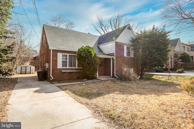 view of front of house with a storage unit, brick siding, roof with shingles, and an outdoor structure