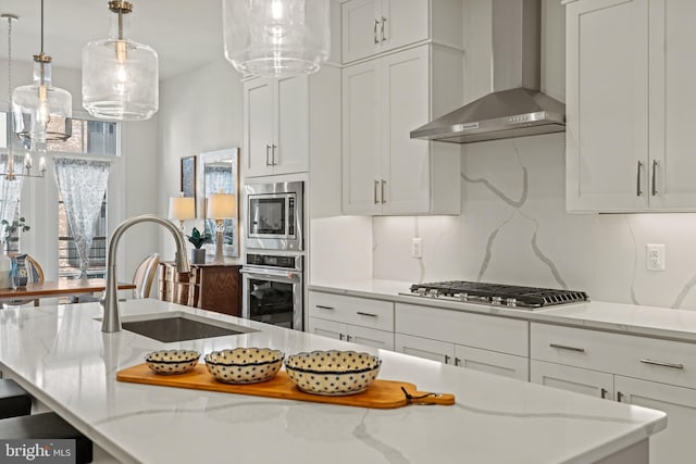 kitchen featuring a sink, tasteful backsplash, appliances with stainless steel finishes, wall chimney range hood, and light stone countertops