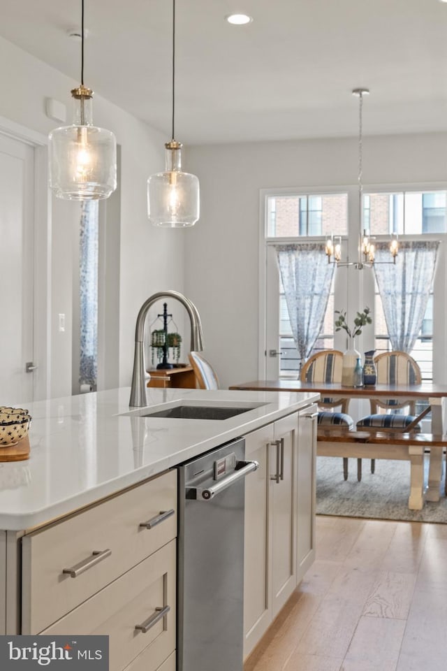 kitchen with a sink, stainless steel dishwasher, white cabinetry, light wood finished floors, and hanging light fixtures