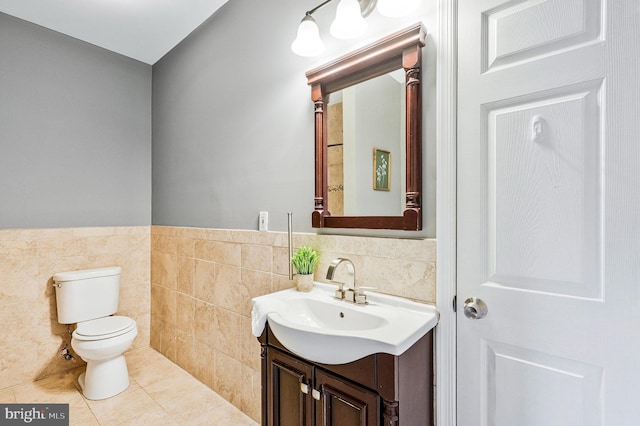 bathroom with a wainscoted wall, toilet, tile walls, tile patterned flooring, and vanity