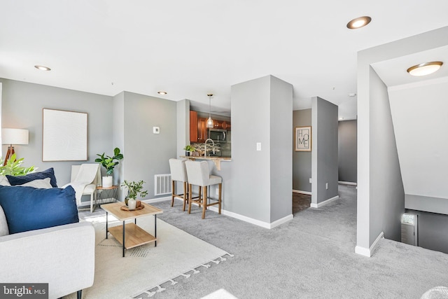 carpeted living area featuring recessed lighting, baseboards, visible vents, and a sink