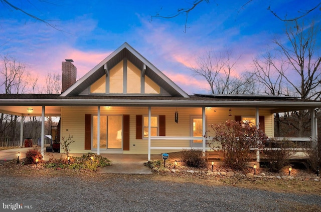 view of front of home with a carport, covered porch, driveway, and a chimney