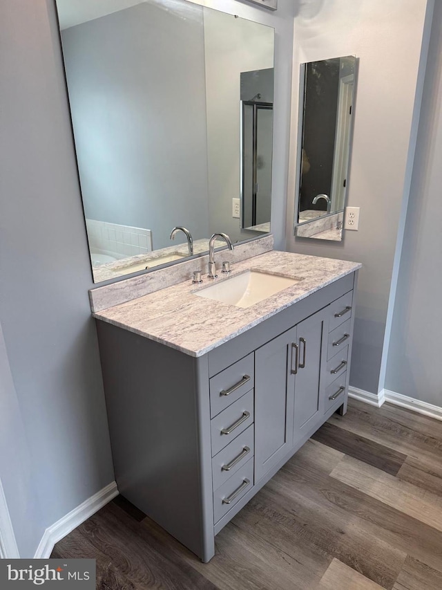 bathroom with vanity, a shower with shower door, wood finished floors, and baseboards