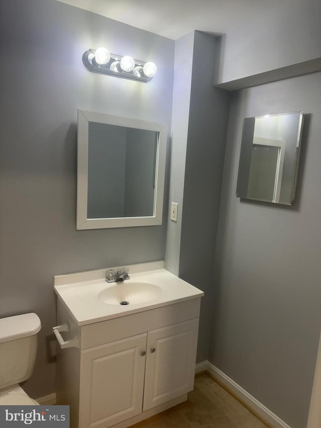 half bathroom with vanity, toilet, and baseboards