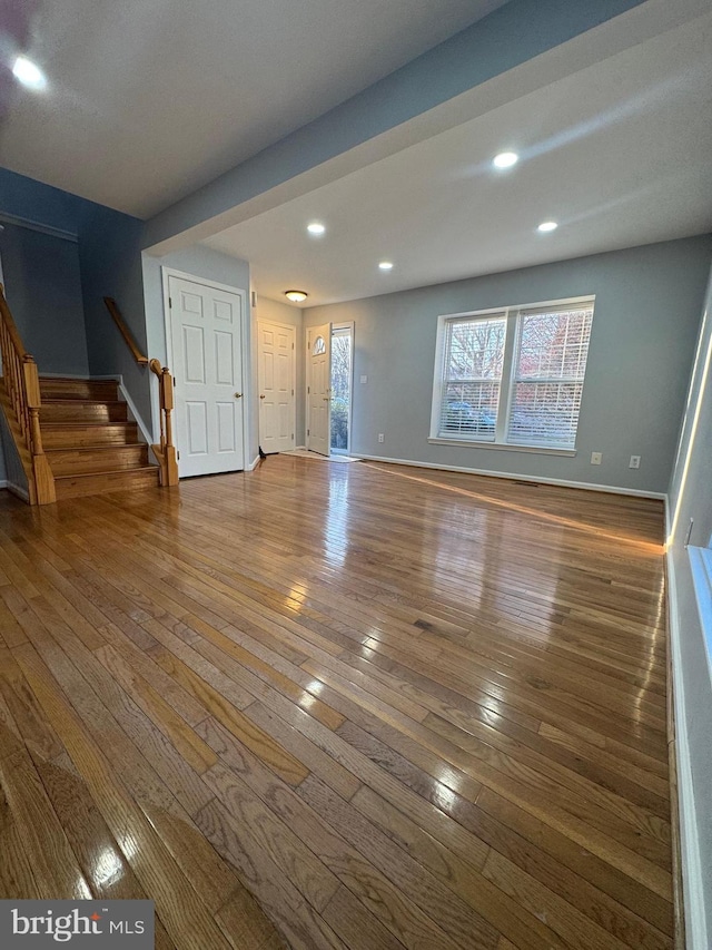 unfurnished living room featuring recessed lighting, stairs, baseboards, and wood-type flooring