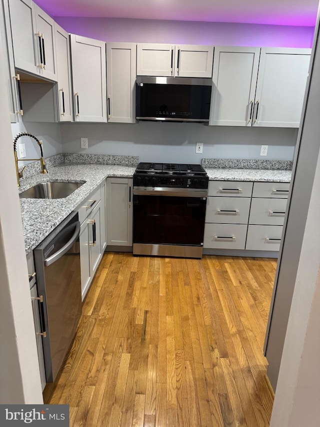 kitchen with a sink, stainless steel dishwasher, light wood finished floors, light stone countertops, and black range with gas stovetop