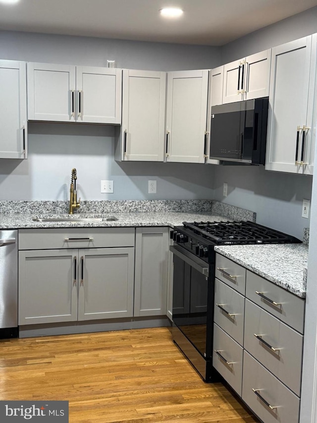 kitchen with light stone counters, light wood-type flooring, appliances with stainless steel finishes, and a sink