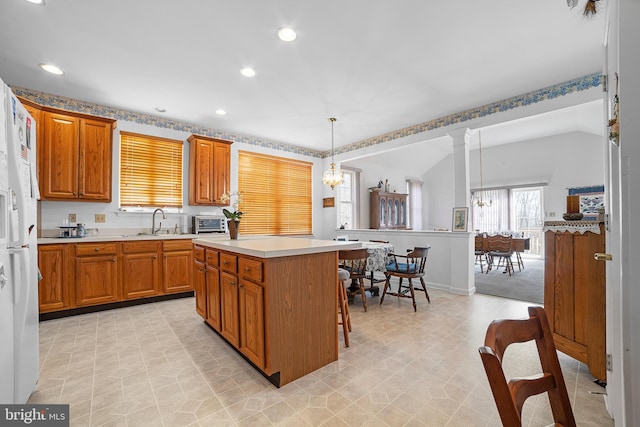 kitchen with brown cabinetry, a kitchen island, a sink, light countertops, and a notable chandelier