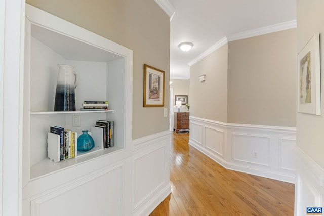 corridor featuring a wainscoted wall, a decorative wall, light wood-type flooring, and ornamental molding