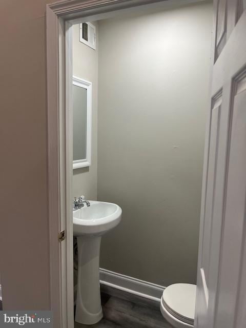 half bath with visible vents, baseboards, toilet, and wood finished floors