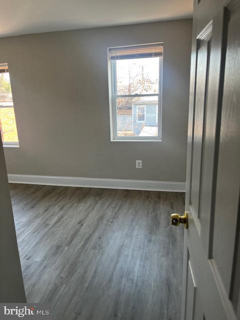 spare room featuring baseboards, dark wood-type flooring, and a healthy amount of sunlight