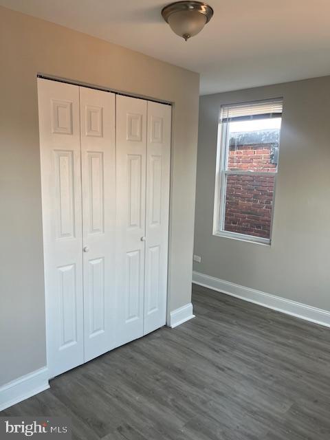 unfurnished bedroom featuring dark wood-style floors, baseboards, and a closet