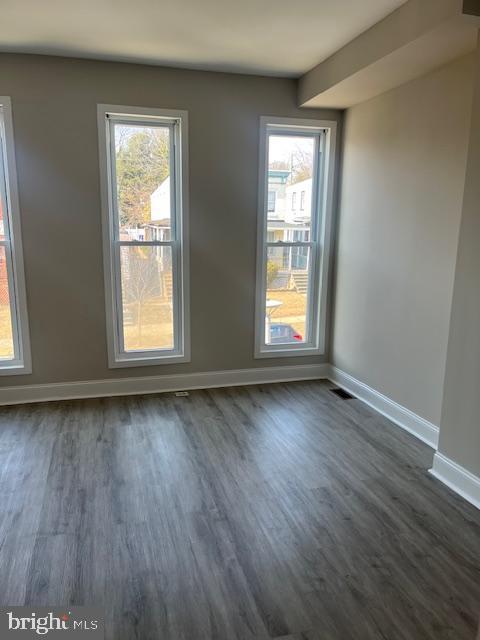 empty room featuring visible vents, baseboards, and dark wood-style flooring