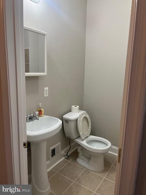 half bath featuring tile patterned flooring, visible vents, toilet, and baseboards