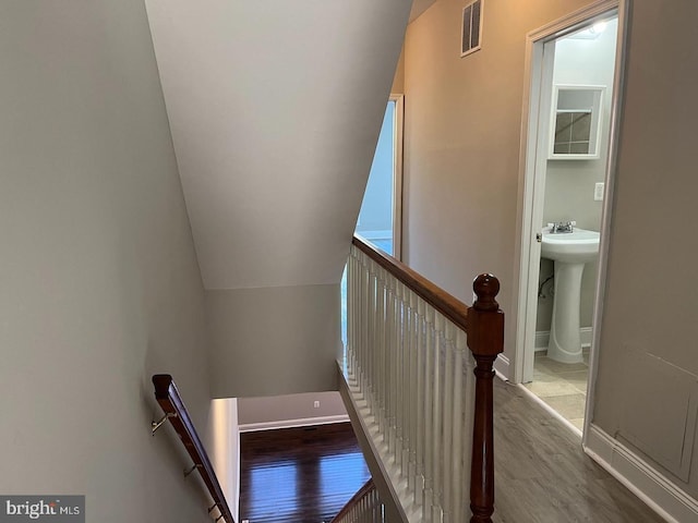 staircase with vaulted ceiling, visible vents, baseboards, and wood finished floors