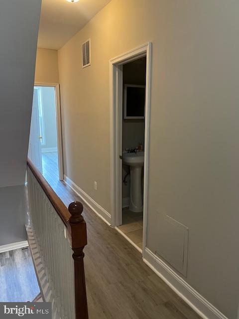 hall with visible vents, baseboards, an upstairs landing, wood finished floors, and a sink