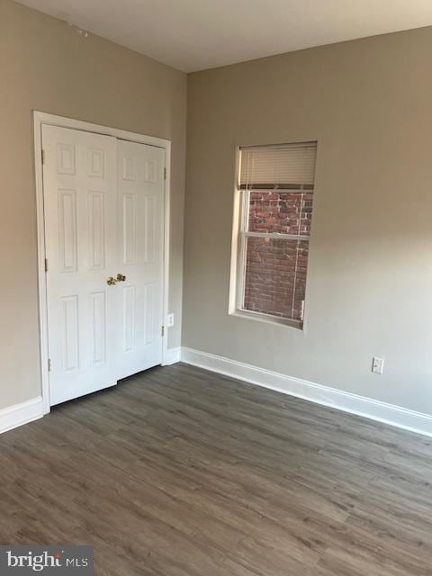 unfurnished bedroom featuring dark wood-style floors, baseboards, and a closet