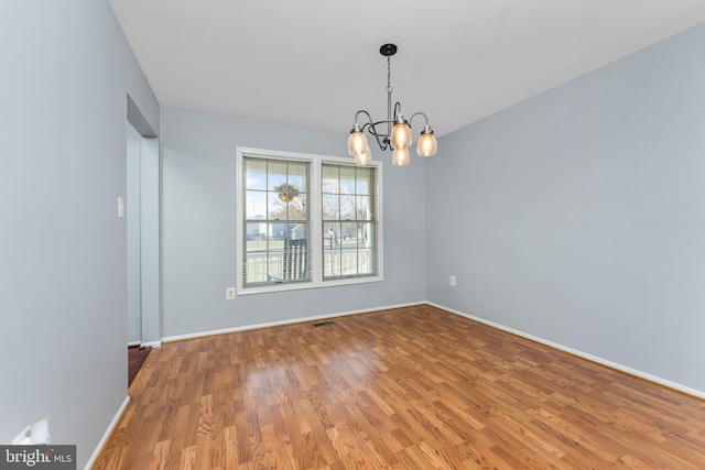 spare room with light wood finished floors, a notable chandelier, visible vents, and baseboards