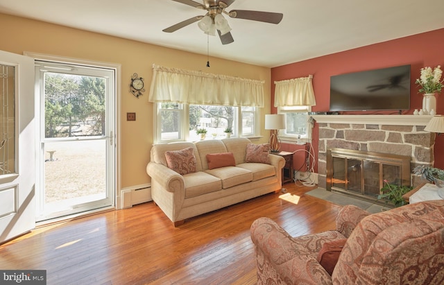 living room featuring plenty of natural light, a stone fireplace, a baseboard heating unit, and hardwood / wood-style floors