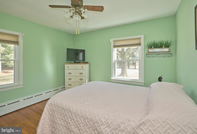 bedroom with multiple windows, baseboard heating, ceiling fan, and dark wood-style flooring