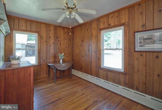 unfurnished dining area featuring ceiling fan, a baseboard radiator, hardwood / wood-style floors, and wood walls