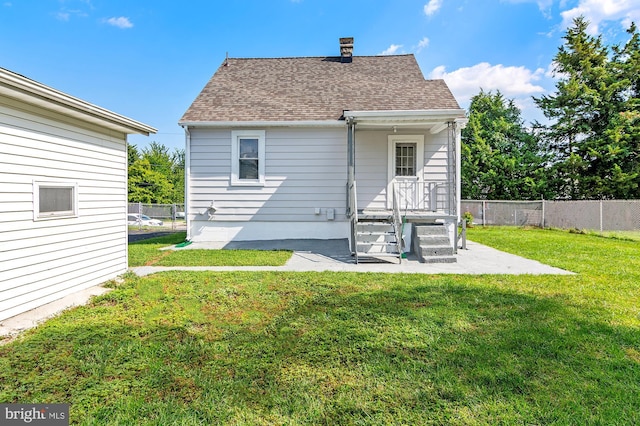 back of property featuring a chimney, a lawn, a shingled roof, and fence