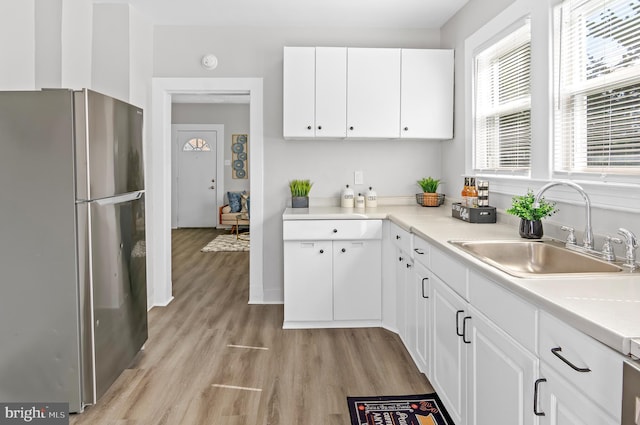 kitchen with light wood finished floors, light countertops, freestanding refrigerator, white cabinets, and a sink