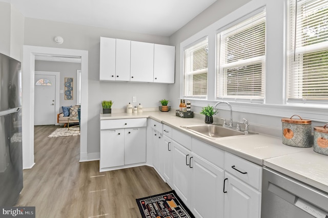 kitchen with a sink, stainless steel dishwasher, white cabinets, and freestanding refrigerator