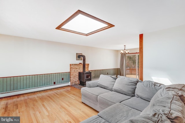 living area featuring light wood-style flooring, a skylight, wainscoting, baseboard heating, and a wood stove