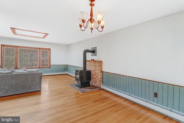 unfurnished living room with a wainscoted wall, baseboard heating, wood finished floors, and a wood stove