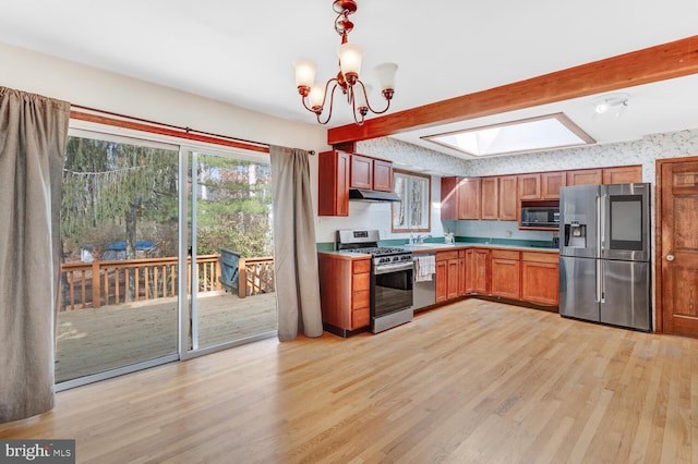 kitchen with beam ceiling, appliances with stainless steel finishes, a skylight, and light wood-style floors