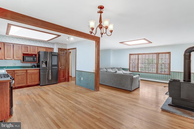 kitchen featuring gas stove, refrigerator with ice dispenser, wainscoting, and black microwave