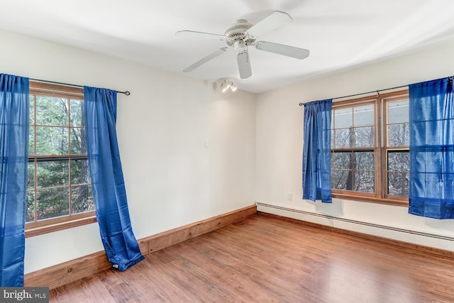 empty room featuring ceiling fan, a baseboard heating unit, baseboards, and wood finished floors