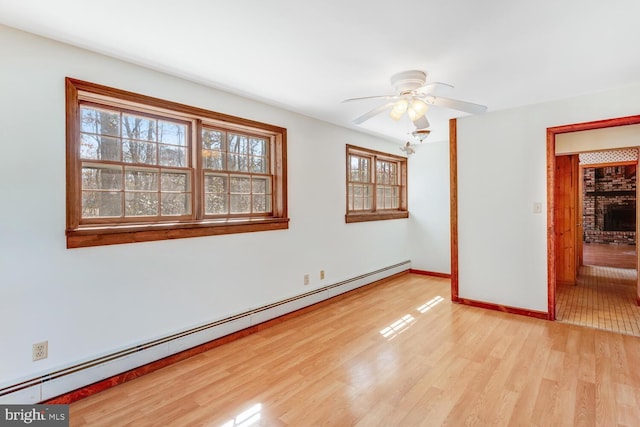 empty room featuring a baseboard heating unit, baseboards, ceiling fan, and light wood finished floors