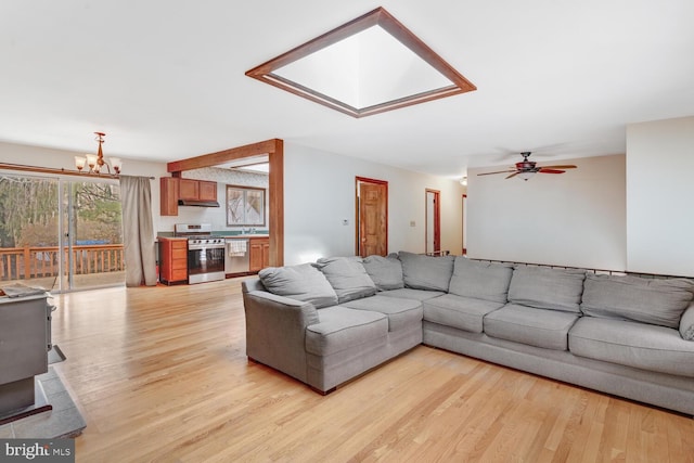 living area featuring ceiling fan with notable chandelier, a skylight, and light wood-type flooring