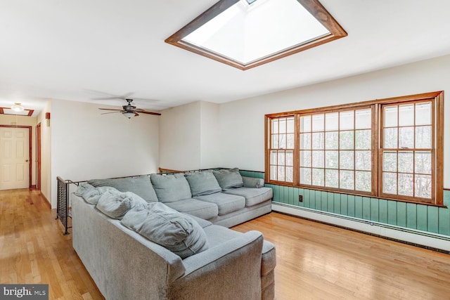 living area with a ceiling fan, a skylight, light wood-style floors, and baseboard heating