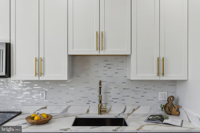 kitchen with tasteful backsplash, stainless steel microwave, light stone countertops, white cabinets, and a sink