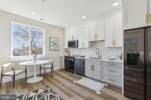 kitchen with a sink, tasteful backsplash, light wood-style floors, appliances with stainless steel finishes, and light countertops