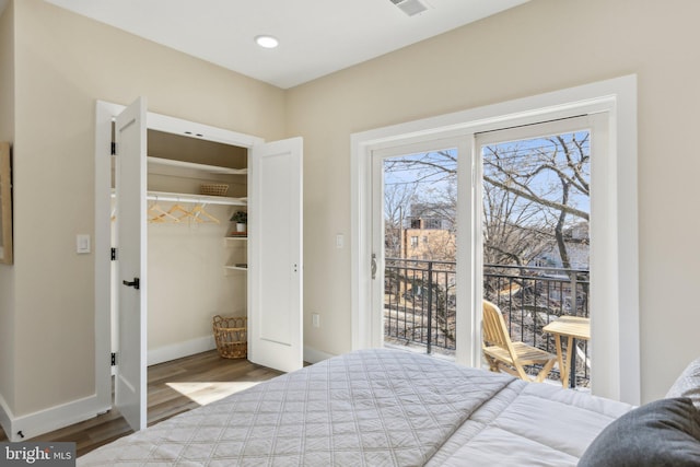 bedroom featuring wood finished floors, a walk in closet, baseboards, and access to outside