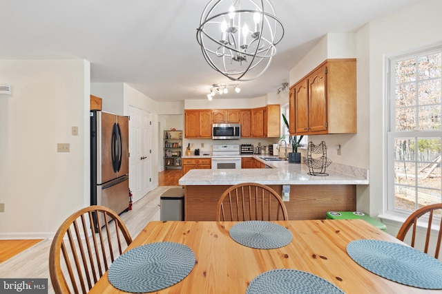 kitchen with light countertops, a peninsula, a notable chandelier, stainless steel appliances, and a sink