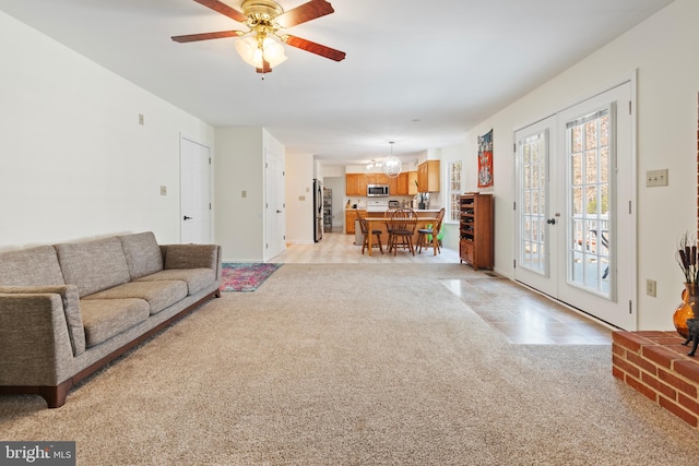 living area featuring light tile patterned flooring, light colored carpet, french doors, and ceiling fan with notable chandelier