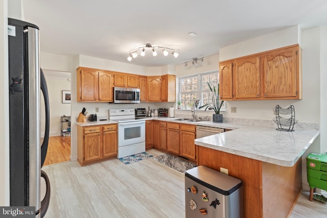 kitchen with light countertops, brown cabinets, a peninsula, stainless steel appliances, and a sink