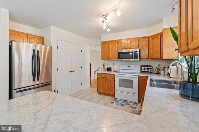 kitchen with a sink, stainless steel appliances, brown cabinetry, and light countertops