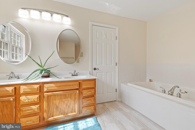 full bathroom with double vanity, wood finished floors, a garden tub, and a sink