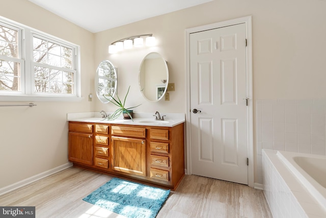 full bathroom featuring a sink, wood finished floors, tiled bath, double vanity, and baseboards